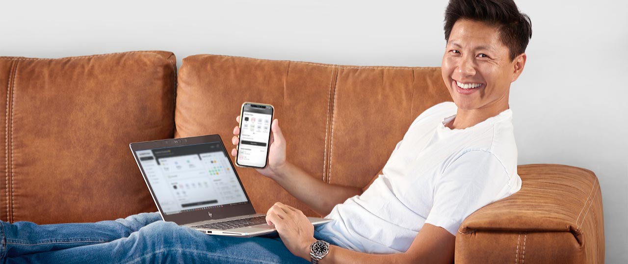 Hombre en un sofá sujetando un smartphone y un portátil para grabar el tiempo de trabajo móvil desde casa.